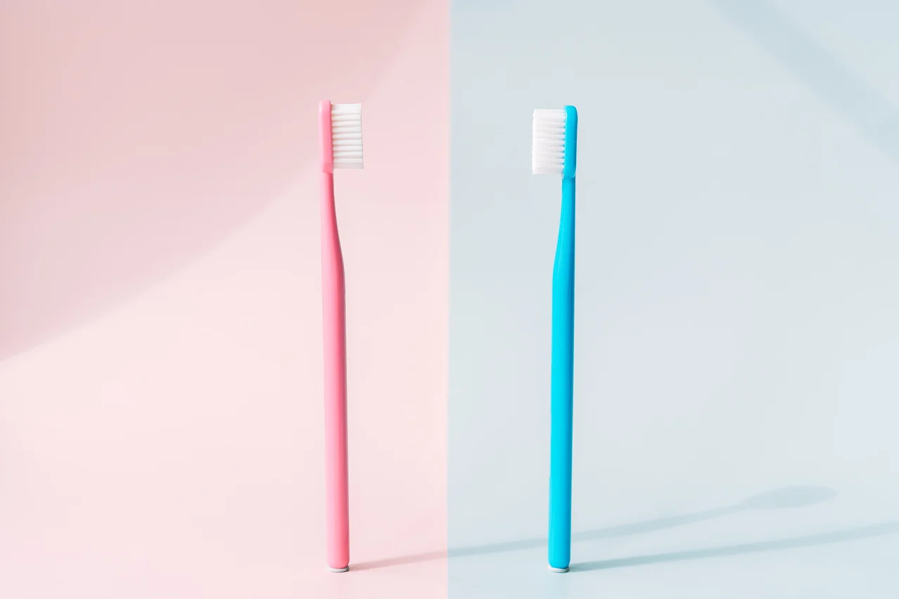 Dos cepillos de dientes que se ven de frente, uno color rosa y otro color celeste