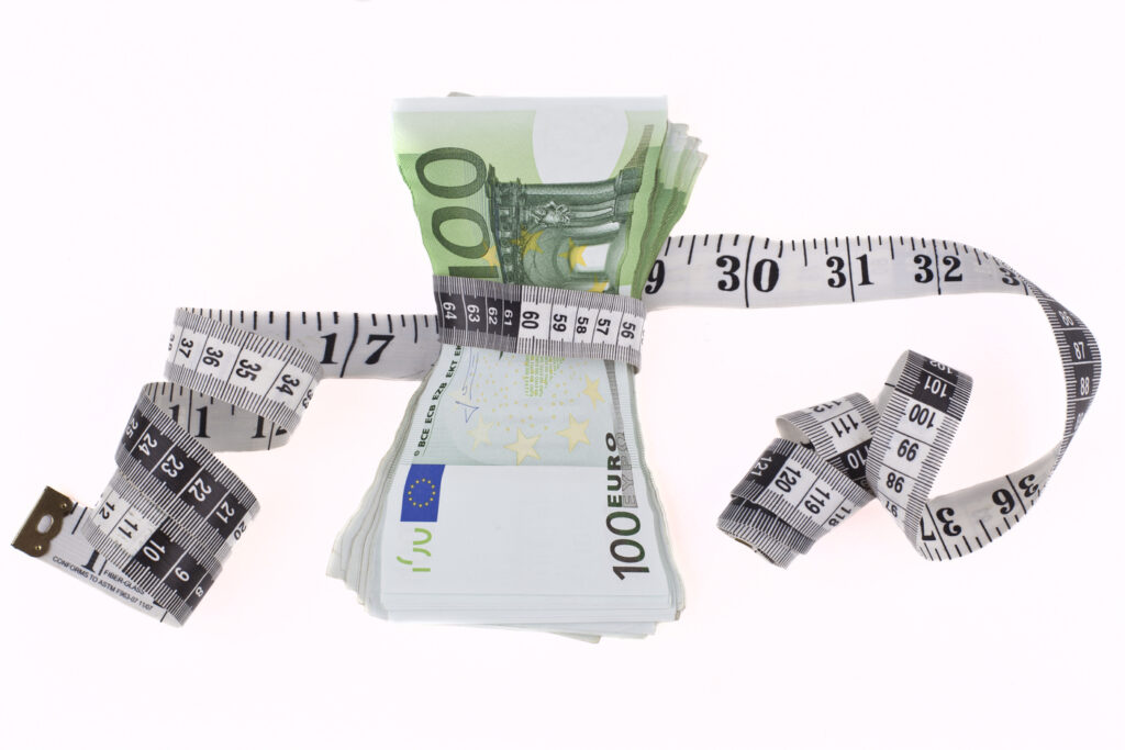 Un manojo de euros siendo encogidos por una cinta métrica